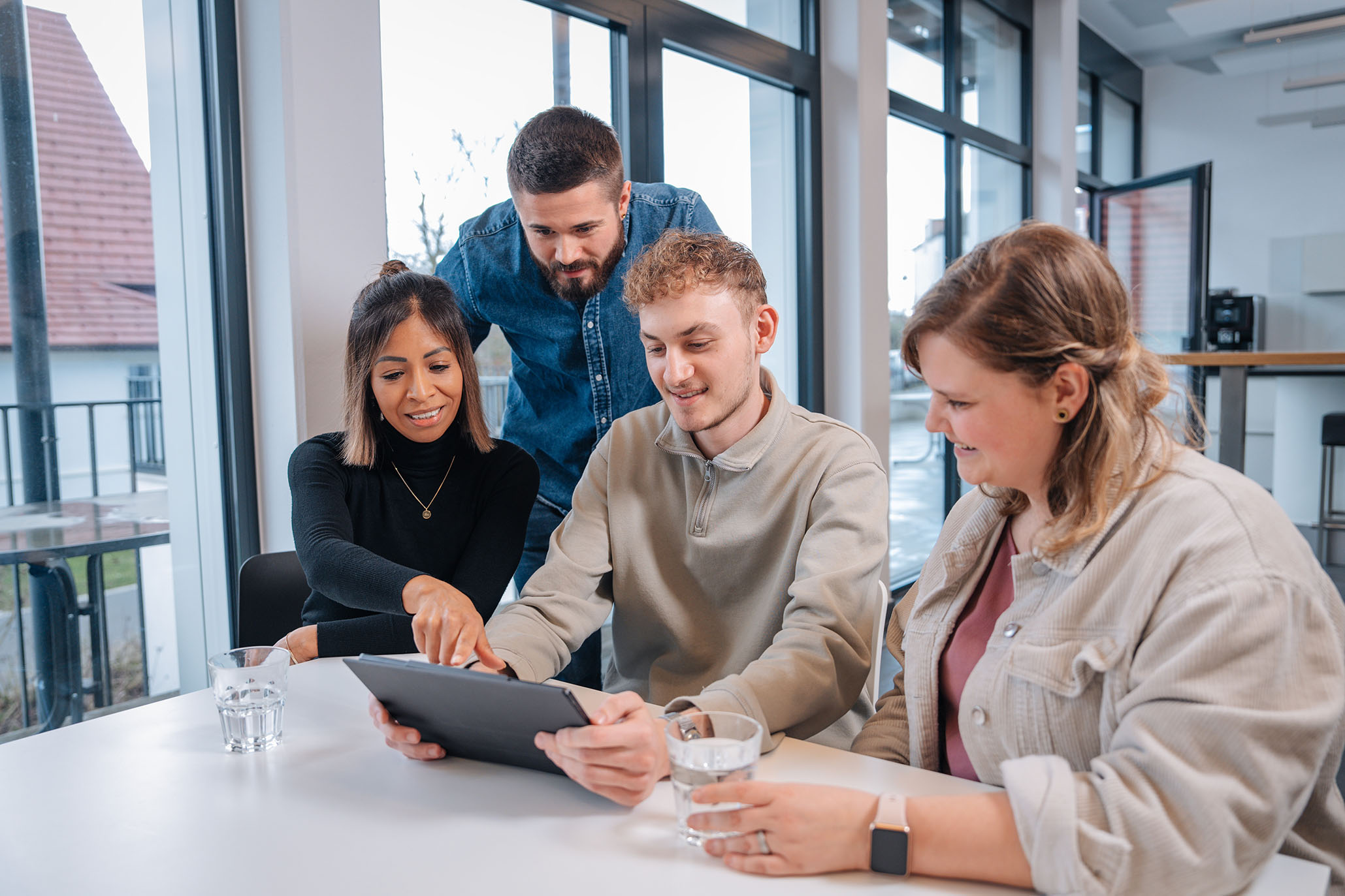 ein Junges Team sitzt gemeinsam am Tisch und beraten sich mit einem Ipad