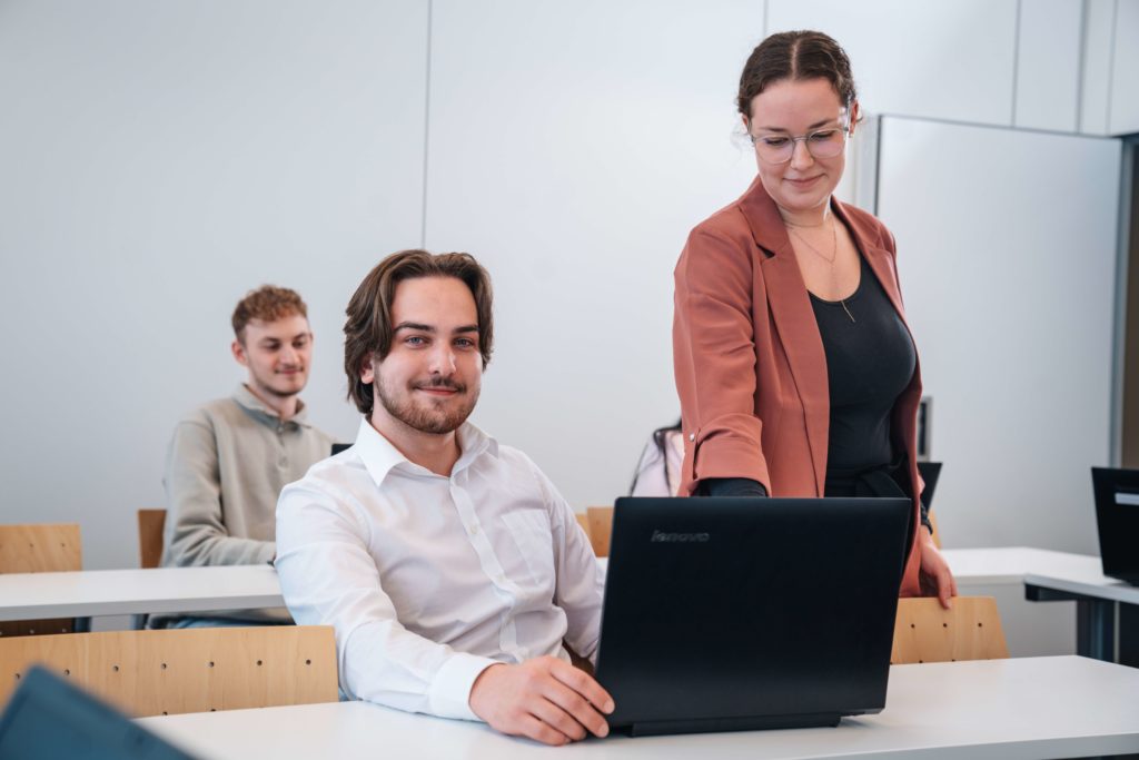 ein Student kriegt etwas an seinem Laptop gezeigt von der Lehrkraft.